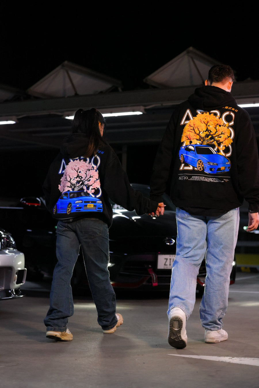 Two people in Sydney Aero Parts JDM hoodies walking through a car park