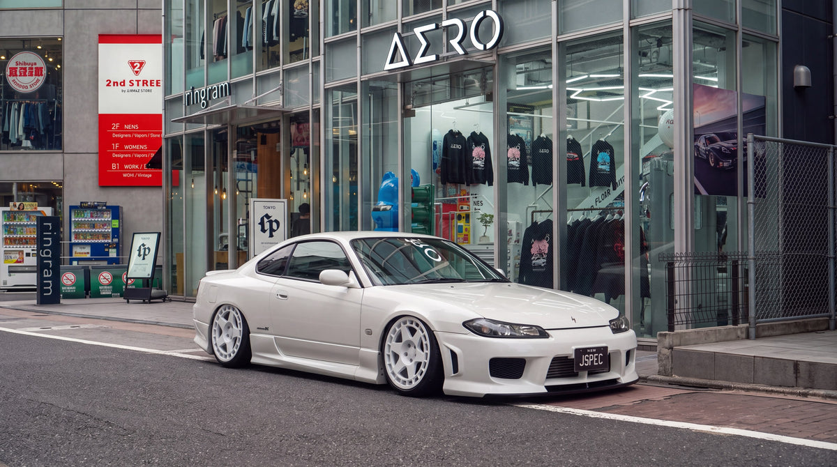 White Nissan S15 Silvia on white wheels parked outside a store window lined with Sydney Aero Parts hoodies