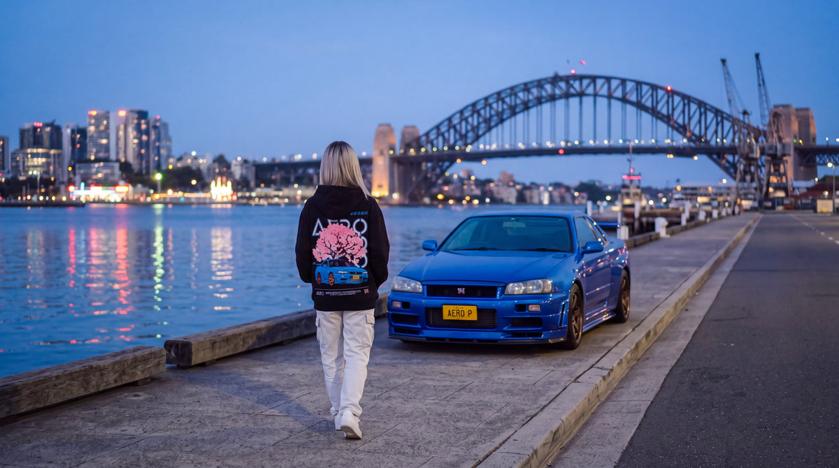 The Skyline Hoodie on the Sydney harbour foreshore at blue hour, with a Bayside Blue R34 GT-R parked beside her