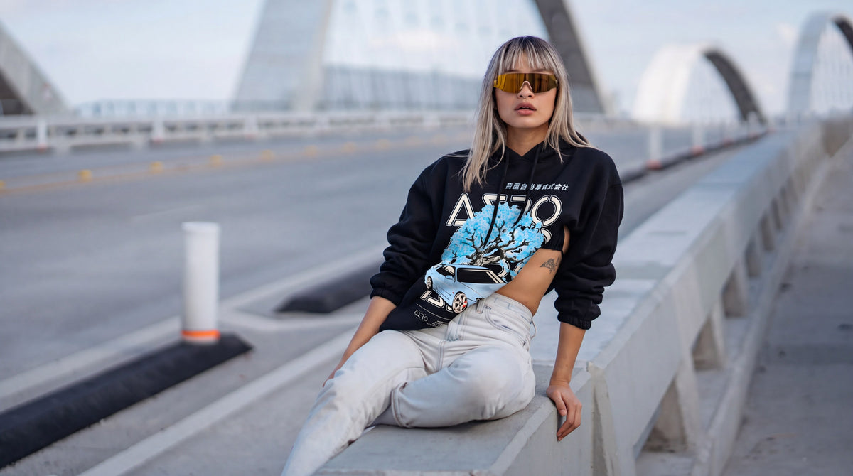 Woman in the black Tiffany hoodie with the blue blossom S15 print, sitting on a bridge barrier